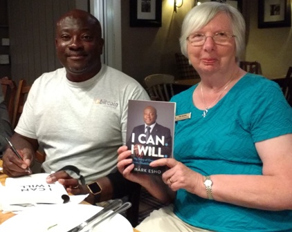 Novus Rotarian Mark Esho signs a copy of his book with Novus secretary Pam spokes holding another copy